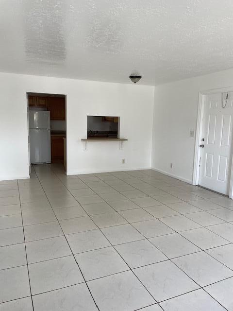 unfurnished living room featuring a textured ceiling, light tile patterned floors, and baseboards