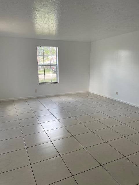 unfurnished room with light tile patterned flooring, a textured ceiling, and baseboards