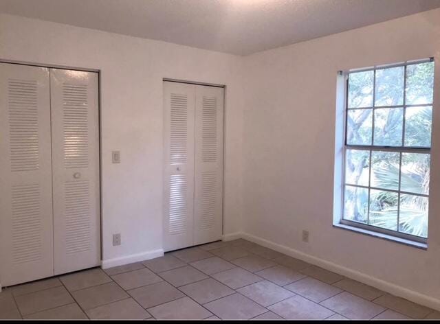 unfurnished bedroom with light tile patterned flooring, baseboards, and two closets