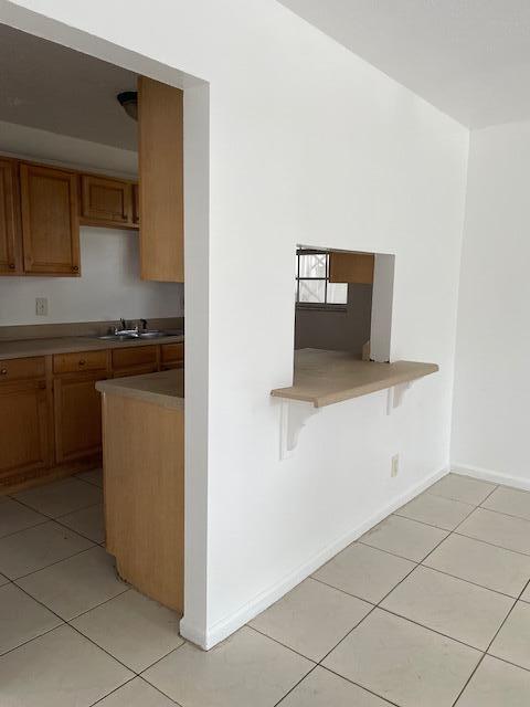 kitchen with a peninsula, brown cabinetry, a sink, and light tile patterned flooring