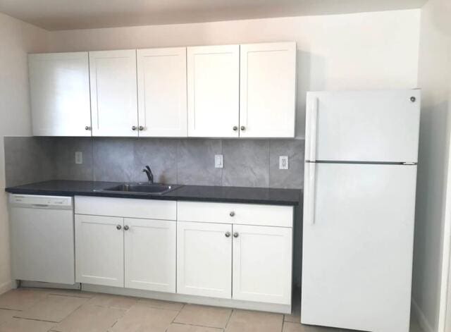 kitchen featuring white appliances, a sink, white cabinets, tasteful backsplash, and dark countertops