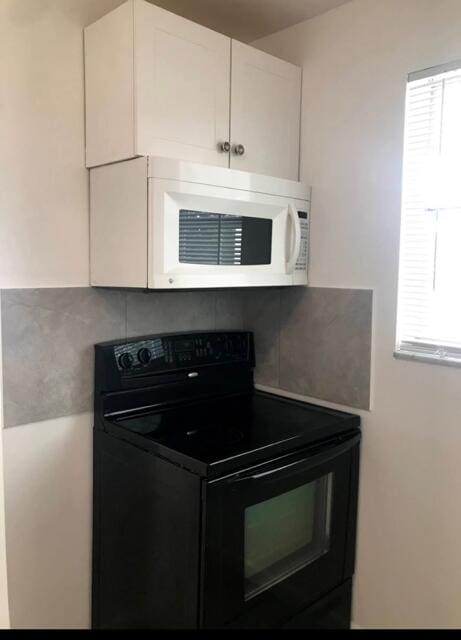 kitchen featuring plenty of natural light, black range with electric cooktop, white microwave, and white cabinetry