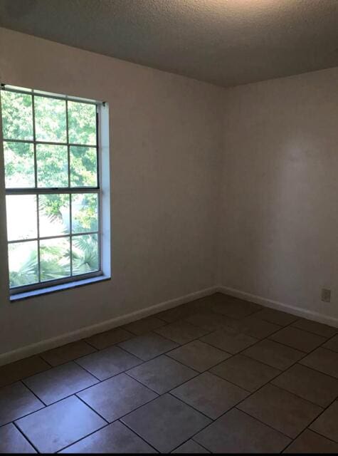 unfurnished room with a textured ceiling, dark tile patterned flooring, and baseboards