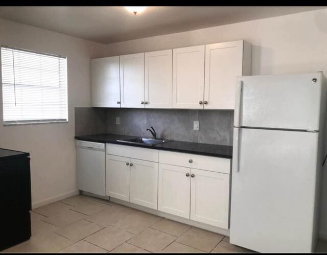 kitchen with white appliances, a sink, white cabinetry, decorative backsplash, and dark countertops