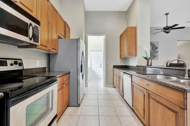 kitchen featuring light tile patterned floors, ceiling fan, a sink, appliances with stainless steel finishes, and brown cabinets