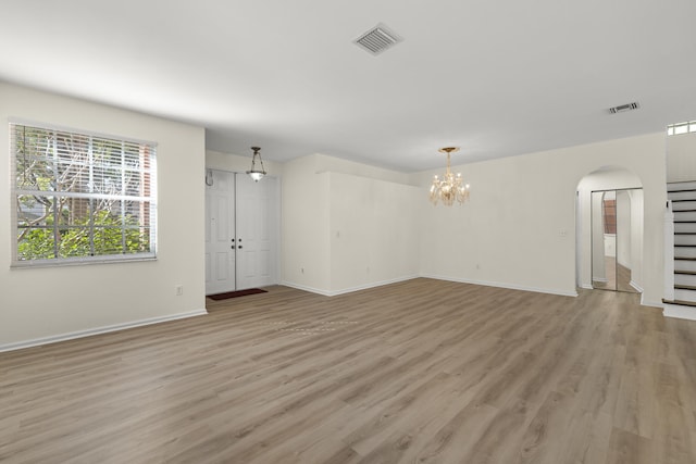 unfurnished living room featuring light wood-type flooring, baseboards, visible vents, and arched walkways