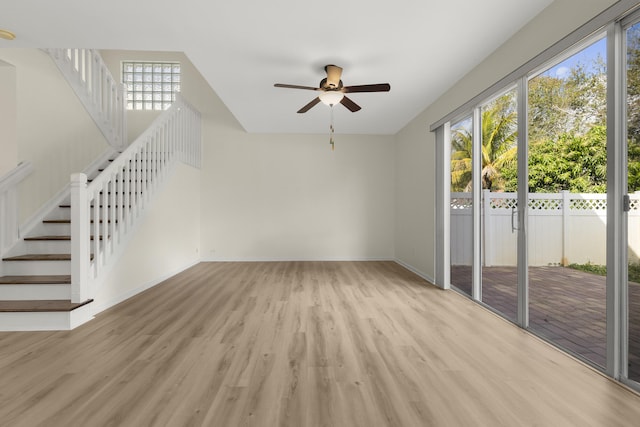 unfurnished living room featuring a ceiling fan, light wood-type flooring, stairway, and baseboards