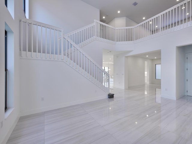 interior space with a towering ceiling, visible vents, stairs, marble finish floor, and baseboards