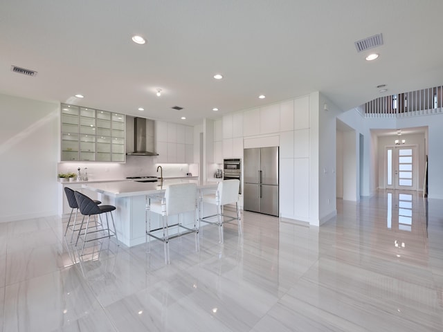 kitchen featuring a breakfast bar area, visible vents, appliances with stainless steel finishes, wall chimney exhaust hood, and modern cabinets