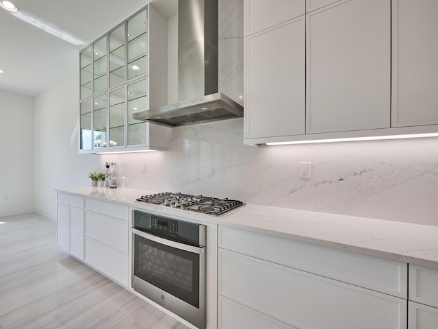 kitchen with stainless steel appliances, wall chimney range hood, and white cabinetry