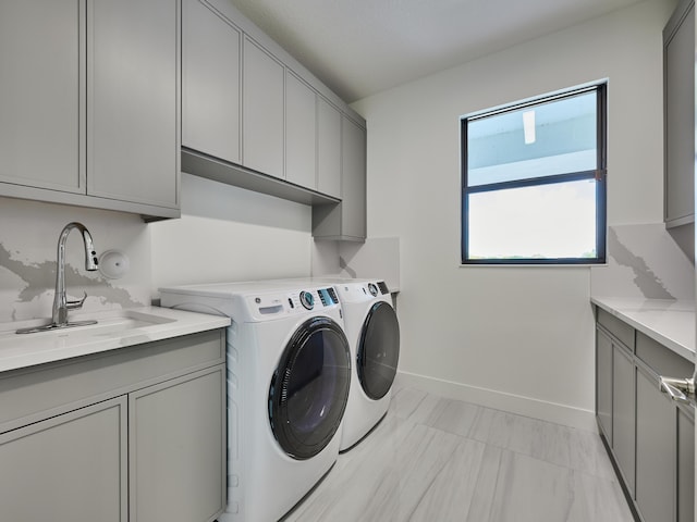 washroom featuring washing machine and dryer, a sink, cabinet space, and baseboards