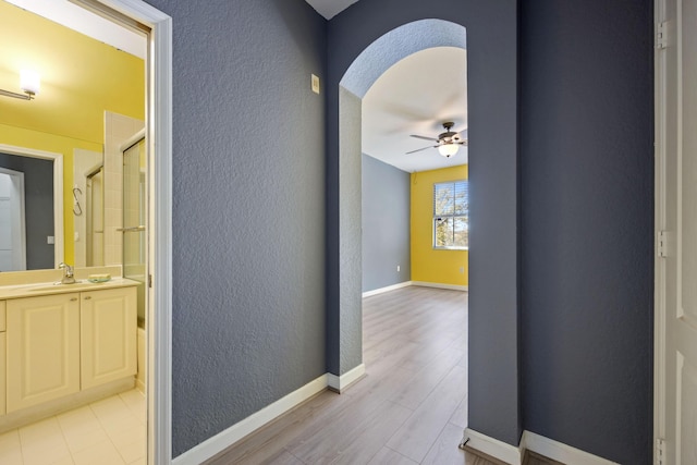 hall with a textured wall, arched walkways, a sink, and baseboards