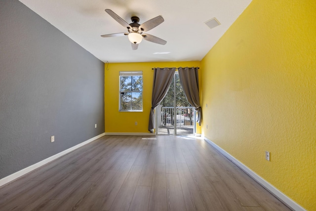 unfurnished room featuring ceiling fan, a textured wall, wood finished floors, visible vents, and baseboards