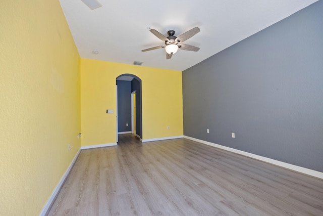 spare room with baseboards, visible vents, a ceiling fan, arched walkways, and wood finished floors