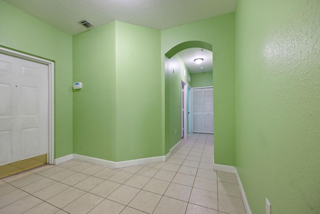 corridor featuring arched walkways, visible vents, baseboards, and light tile patterned flooring