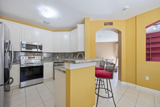 kitchen featuring a peninsula, light tile patterned floors, appliances with stainless steel finishes, and a breakfast bar area