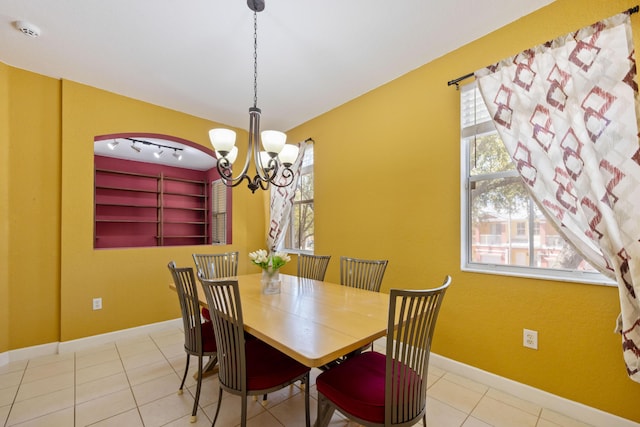 tiled dining space featuring a chandelier, rail lighting, and baseboards