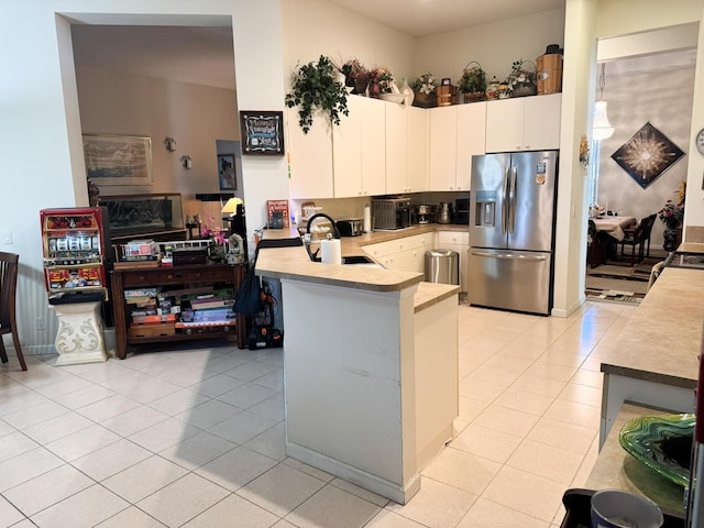 kitchen featuring light tile patterned floors, a peninsula, stainless steel refrigerator with ice dispenser, and a sink