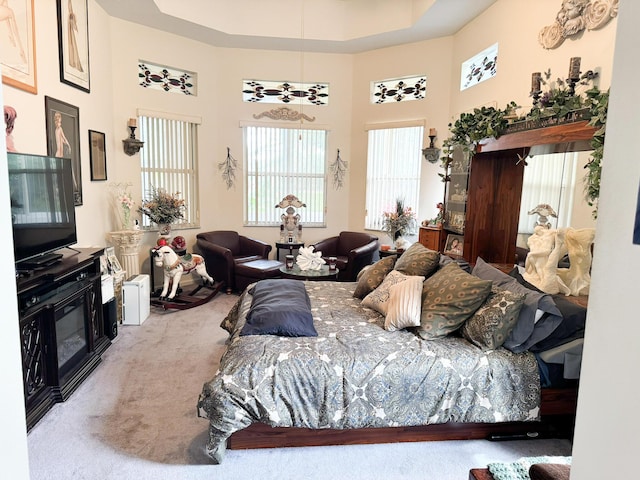 carpeted bedroom with a tray ceiling, a high ceiling, and a glass covered fireplace