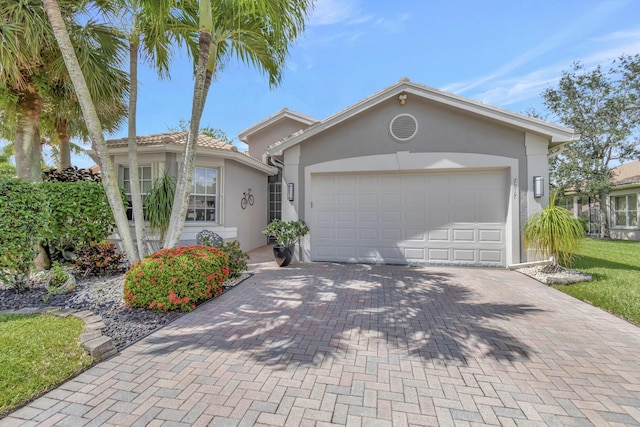 view of front of home featuring an attached garage, a tiled roof, decorative driveway, and stucco siding