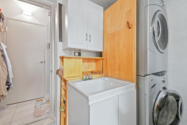 washroom with cabinet space, a textured wall, a textured ceiling, and stacked washing maching and dryer