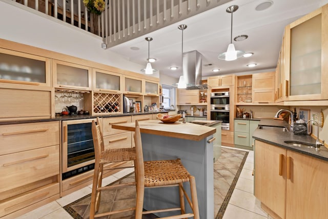 kitchen with wine cooler, island exhaust hood, glass insert cabinets, light brown cabinets, and a sink