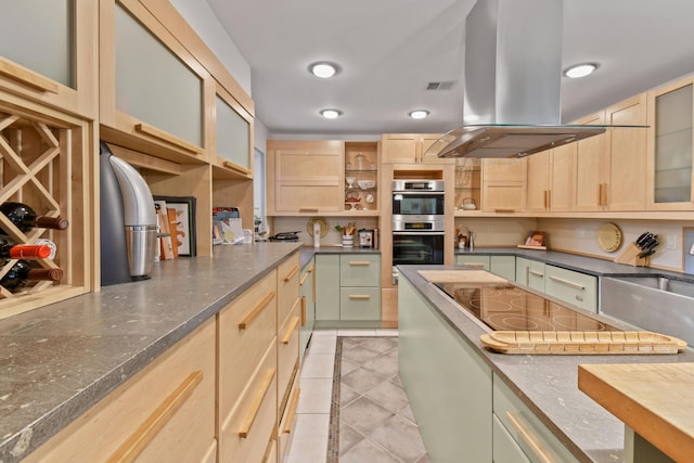 kitchen featuring island exhaust hood, light brown cabinetry, glass insert cabinets, stainless steel double oven, and light tile patterned flooring