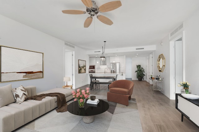 living area featuring visible vents, ceiling fan, light wood-style flooring, and baseboards