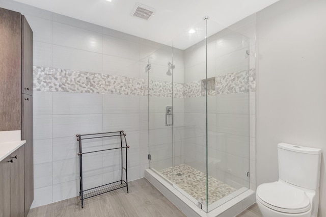 full bathroom featuring toilet, vanity, visible vents, tile walls, and a stall shower