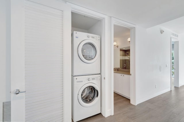 laundry area with stacked washer / drying machine, laundry area, light wood-style flooring, and baseboards