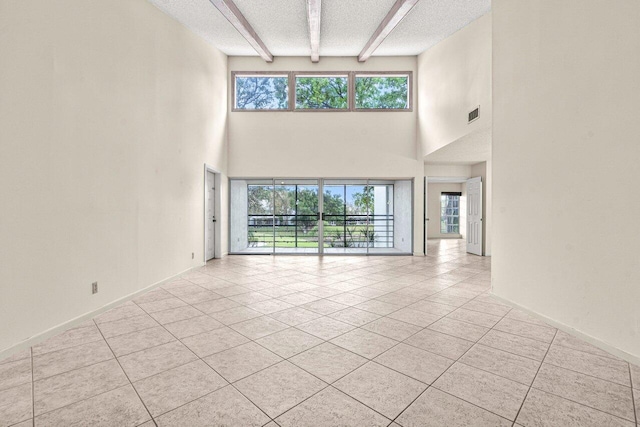 unfurnished living room featuring a wealth of natural light, a textured ceiling, light tile patterned floors, and beam ceiling