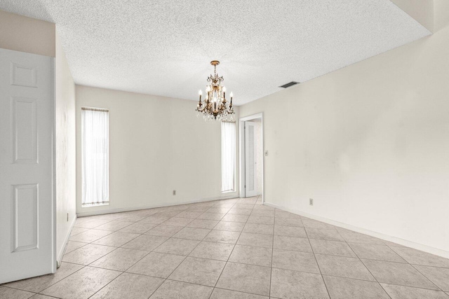 unfurnished room featuring visible vents, an inviting chandelier, light tile patterned flooring, a textured ceiling, and baseboards