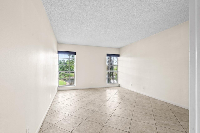 spare room featuring light tile patterned floors, baseboards, and a textured ceiling