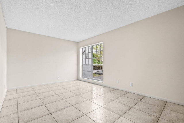 spare room featuring a textured ceiling, baseboards, and light tile patterned floors