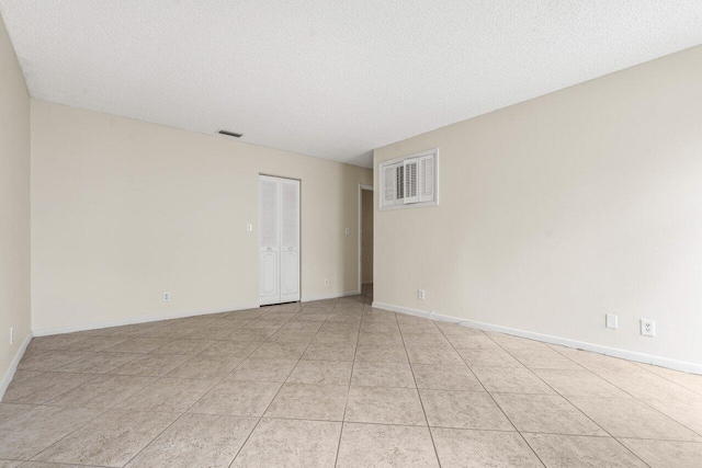 empty room featuring light tile patterned floors, a textured ceiling, visible vents, and baseboards