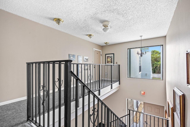 stairway with a chandelier, carpet floors, a textured ceiling, and baseboards