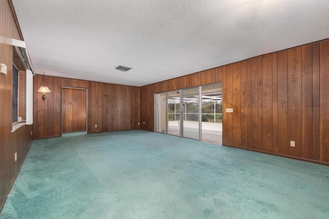 unfurnished room with wooden walls, a textured ceiling, visible vents, and carpet flooring