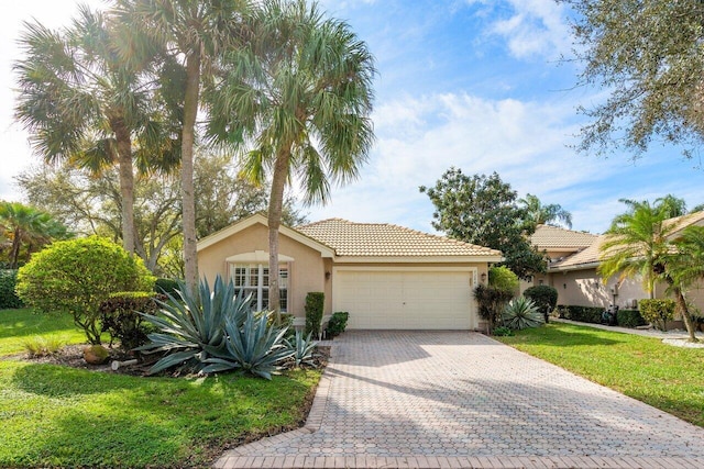 view of front of home featuring an attached garage, a tile roof, decorative driveway, stucco siding, and a front lawn