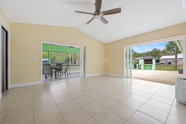 tiled empty room with vaulted ceiling, plenty of natural light, baseboards, and ceiling fan