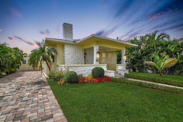 view of front of property featuring a porch, stone siding, stucco siding, a chimney, and a front yard