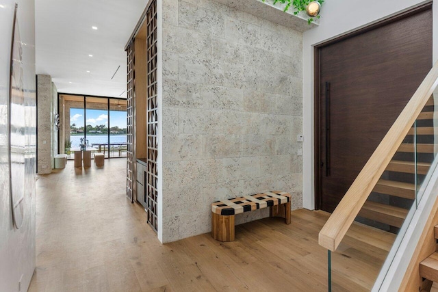 hallway with stairway, a wall of windows, a water view, and wood finished floors