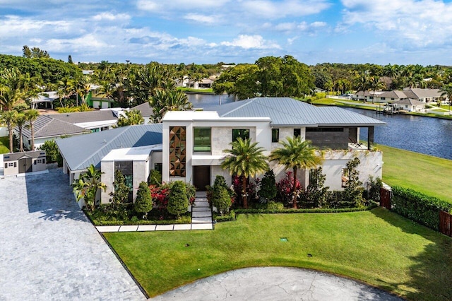 contemporary house featuring a water view, a front yard, metal roof, fence, and a residential view