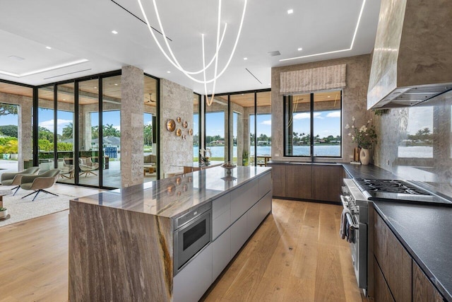 kitchen with stainless steel appliances, wall chimney range hood, light wood-type flooring, floor to ceiling windows, and modern cabinets