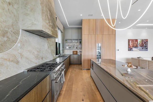 kitchen with light wood-type flooring, modern cabinets, dark stone counters, and range with two ovens