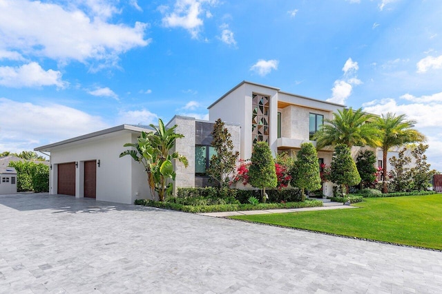 modern home with an attached garage, decorative driveway, a front yard, and stucco siding