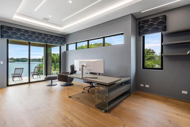 office space with a tray ceiling, a water view, wood finished floors, and visible vents