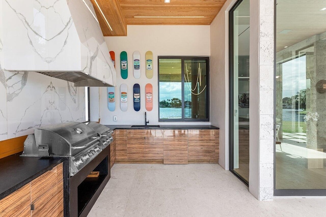 kitchen featuring tasteful backsplash, wooden ceiling, brown cabinets, and under cabinet range hood