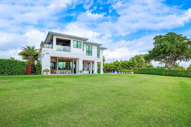 rear view of property with a lawn, a balcony, and stucco siding