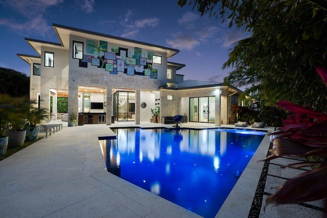 back of property at dusk featuring exterior kitchen, a patio area, an outdoor pool, and stucco siding