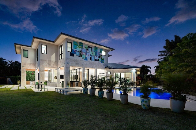 back of property at dusk featuring stucco siding, a lawn, a patio area, stone siding, and an outdoor pool